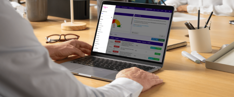 A person using a laptop at a desk, viewing a dashboard with charts, lists, and navigation menus related to Recommended Safety Software. Other people are seated at the table in the background.