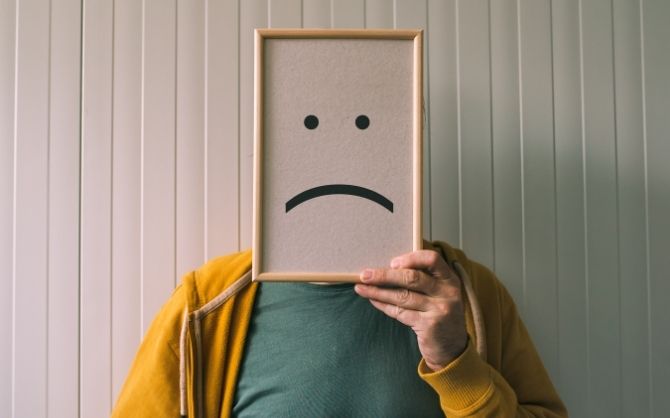 A person, striving to manage psychosocial hazards, holds a picture frame with a sad face drawing.